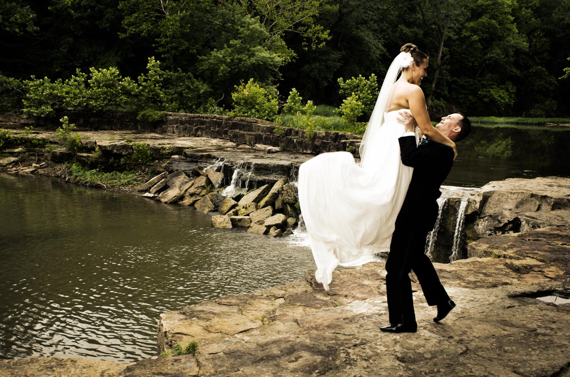 Barely married couple burst into spontaneous laughter when the groom surprises the bride by throwing her up into the air, by Robertsons' Warehouse Photography, Wichita, KS